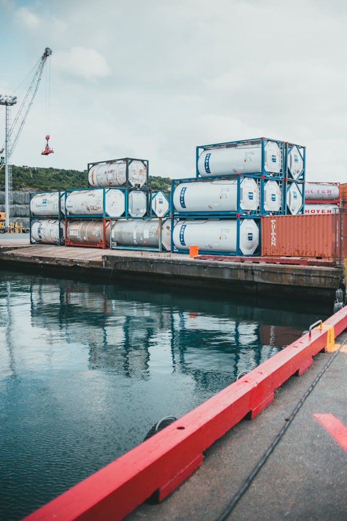 A view of shipping containers stacked at a commercial dock with a crane in the background.